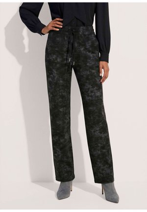 Persoon draagt zwarte en grijze camouflagebroek met trekkoord, grijze suède enkellaarsjes met hoge hak en een zwarte top met lange mouwen.