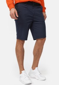 Marineblaue Baumwollshorts mit seitlichen Taschen, taillierter Passform und Abschlüssen, kombiniert mit weißen Sportschuhen.