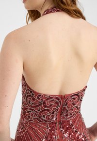 Retro di un abito da sera borgogna caratterizzato da un'argenteria intricata e paillettes, con una profonda scollatura e una chiusura con cerniera al centro retro.