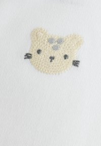 Weißer Baumwollstoff mit einem bestickten Katzenkopf in Beige, Grau und Schwarz, mit Schnurrhaaren und drei Pfotenabdrücken über dem Kopf.