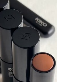 Drei schwarze zylindrische Kosmetikbehälter mit mattem Finish; einer hat einen runden braunen Deckel. Dezentes Branding an den Seiten.