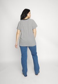 Maglietta a righe bianca e nera con maniche corte e colletto nero, abbinata a jeans a zampa d'elefante blu, vista da dietro.