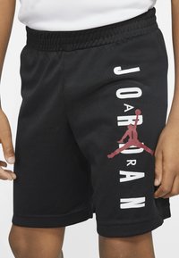 Czarne szorty sportowe z siateczkową teksturą, z białym i czerwonym napisem "JORDAN" oraz logo na lewym nogawce, elastyczny pas.