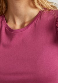 Krótki rękaw, okrągły dekolt, bluzka w jednolitym kolorze mauve z gładkiego materiału, z koronkowymi akcentami na rękawach dla dodatkowego detalu.