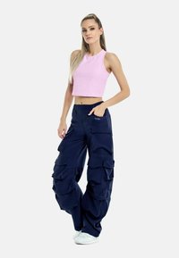 Rosa cropped tank top och navy oversized cargo-byxor med flera fickor. Vita sneakers fulländar outfiten. Slät tygstruktur.