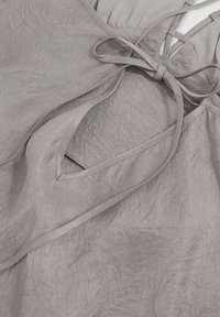 Abito in lino grigio chiaro con una finitura testurizzata, caratterizzato da un design a scollo a V e una schiena legata. Espone un'apertura triangolare lungo il lato.