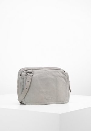 Sac bandoulière en cuir gris clair avec poche avant et bandoulière réglable, posé sur une surface blanche.