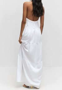 Biała, bezrękawnikowa sukienka maxi o warstwowej konstrukcji, z elastycznym pasem i gładką fakturą. Posiada niski dekolt na plecach i długość do podłogi.
