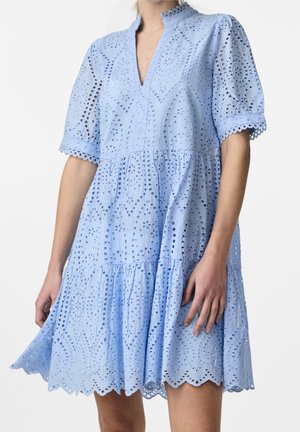 Femme portant une robe en dentelle ajourée bleu clair avec manches courtes bouffantes, bords festonnés et encolure en V, montrée des épaules jusqu'au milieu des cuisses.
