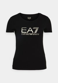 Camiseta de algodón negra con cuello redondo y mangas cortas. En el frontal se muestra un logo metálico plateado: "EA7 EMPORIO ARMANI."