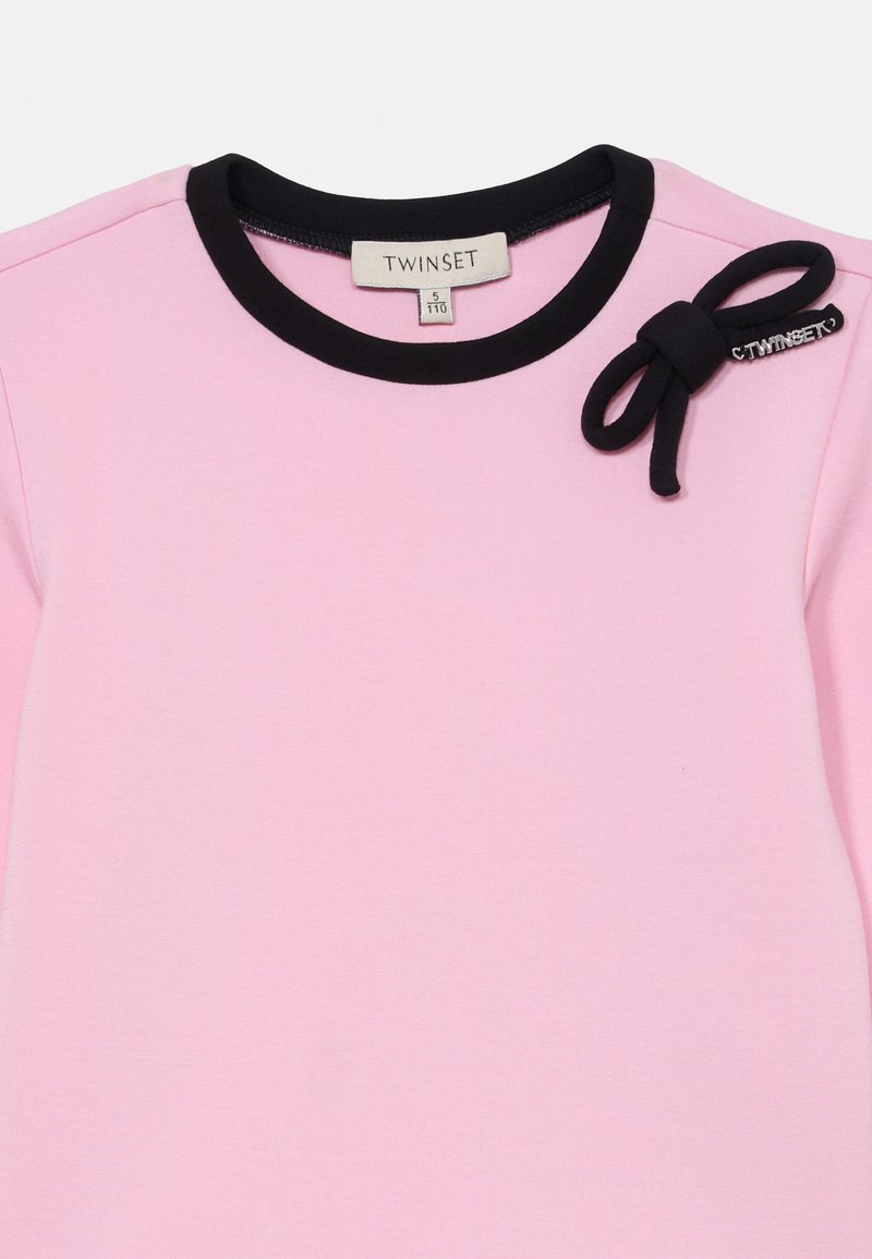 Maglietta rosa a maniche corte con colletto a costine nero, caratterizzata da un elegante fiocco decorativo e dal nome del marchio "TWINSET" ricamato in nero.