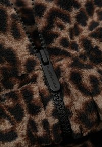 Fleece o wzorze lamparta z czarnym zamkiem błyskawicznym, o miękkiej teksturze w brązowych i beżowych odcieniach.