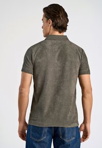 Olijfgroene polo met korte mouwen, met een gladde textuur, een kraagontwerp en zijsplitaccenten, gecombineerd met blauwe spijkerbroeken.