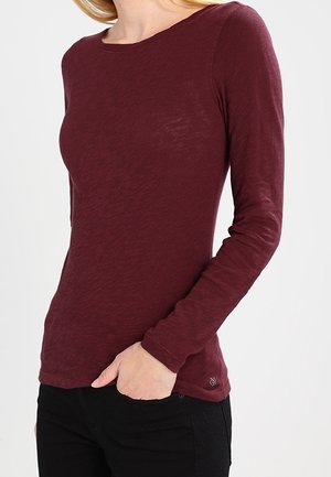 Burgunderfarbiges Langarmshirt mit Rundhalsausschnitt, aus strukturiertem Stoff, mit dezentem Muster und kleinem Logo am Saum.