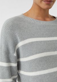 Pull en tricot gris avec de larges rayures horizontales blanches, un col rond et des poignets et un ourlet côtelés. Tissu texturé avec une coupe décontractée.