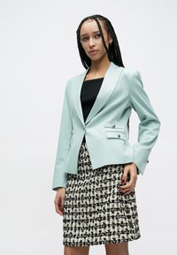 Svetlo modré sako s dvoma prednými vreckami a striebornými gombíkmi, skombinované s čiernym topom a priliehavou čierno-bielou vzorovanou sukňou.