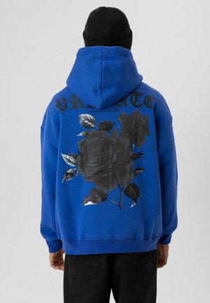 Blauwe hoodie met zwarte rozenafbeeldingen en letters op de achterkant. Zacht materiaal met een relaxte pasvorm en geribbelde manchetten.