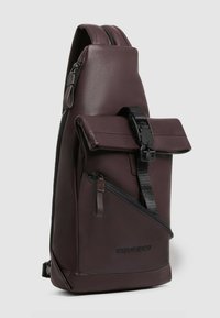 Borsa a tracolla in pelle color bordeaux con patta arrotolata, tasca laterale con zip, tracolla regolabile e logo del marchio in rilievo alla base.