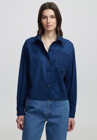 Marineblauwe suède shirt met een kraaghals, lange mouwen, een borstzak met een ingewikkelde textuur en drukknoopsluiting.