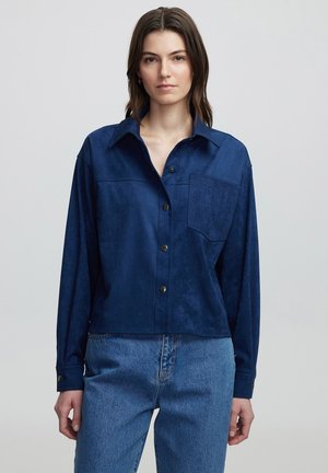 Marineblauwe suède shirt met een kraaghals, lange mouwen, een borstzak met een ingewikkelde textuur en drukknoopsluiting.