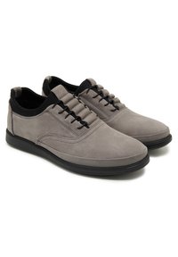 Graue Wildlederschuhe mit einer glatten Oberfläche, schwarzen Akzenten und minimaler Schnürung. Sie haben eine abgerundete Zehenpartie und eine Gummisohle für zusätzlichen Komfort.