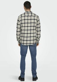 Gecontroleerde flanellen blouse in roomwit en marineblauw met lange mouwen, button-down kraag en een rechte snit, gedragen over een blauwe spijkerbroek.