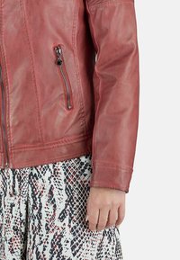 Chaqueta de cuero roja con cremallera frontal, bolsillos laterales y una textura suave. Presenta un diseño ajustado y costuras en contraste.