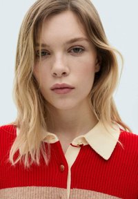 Röd och krämfärgad ribbad stickad tröja med krage och knappstängning. Mjuk textur med ränder i olika nyanser.