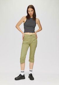 Černo-bíle pruhovaný crop top, olivově zelené capri kalhoty, černé tenisky a bílé ponožky s černými pruhy; casual, přiléhavý design.
