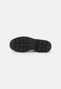 Suela de zapato de goma negra con diseño de banda de rodadura robusto, que presenta profundas ranuras y patrones en forma de estrella para una mejor adherencia y tracción.