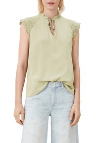 Blusa sin mangas de color verde claro con detalles de encaje en los hombros, cierre con lazo en el cuello y tejido suave y liso. Combinada con denim claro.