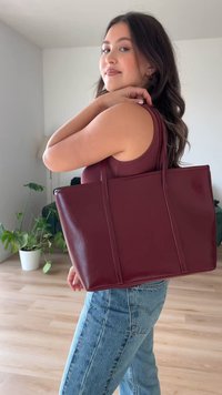 Καφέ δερμάτινη τσάντα tote με δύο μακριά χερούλια, ορθογώνιο σχήμα, γυαλιστερή υφή και ενισχυμένες ραφές. Φοριέται στον ώμο ενός μοντέλου.