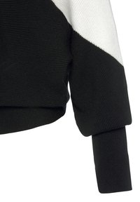 Black and white knit sweater detail featuring ribbed texture, diagonal color blocking, and a loose-fitting sleeve with a cuff.