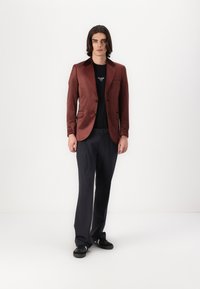 Blazer burdeos con acabado satinado, solapas con muesca, camiseta negra, pantalones gris oscuro y zapatillas negras. Textura suave, corte ajustado.
