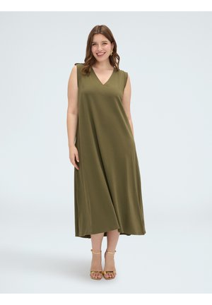 Lachende vrouw in een mouwloze olijfgroene midi-jurk met V-hals en gouden enkellint hakken, staand op een effen witte achtergrond.