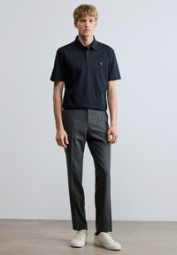 Tengerészkék rövid ujjú galléros póló kis logóval, szürke szabott nadrággal és fehér tornacipővel párosítva. Sima anyag és tiszta vonalak.