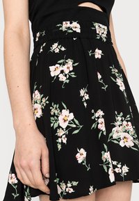 Gonna nera floreale con una vita arricciata, caratterizzata da fiori rosa e bianchi e foglie verdi. Tessuto leggero con una texture morbida.