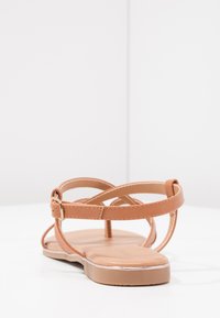 Tan leather sandal with a flat sole, crisscross straps, adjustable buckle, and a smooth finish. Side view showing minimal design.