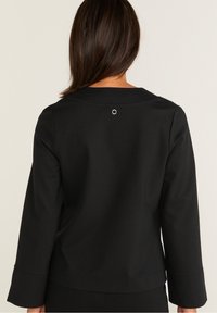 Černý top s dlouhými rukávy, kulatým výstřihem, jemným materiálem a stříbrným detailem na zadní straně poblíž výstřihu.