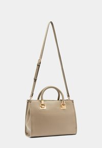 Sac à main en cuir beige avec une forme structurée, des poignées supérieures tressées et des accents en métal doré. Inclut une bandoulière détachable.
