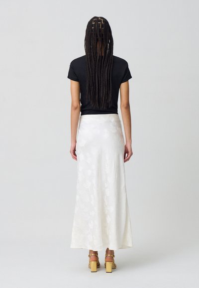Camiseta negra ajustada combinada con una falda larga de satén blanca con estampado floral, que presenta una textura suave y sandalias amarillas de tacón cuadrado.