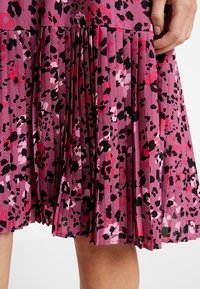 Faltenrock aus lila Stoff mit einem pinken und schwarzen abstrakten Muster. Verfügt über ein fließendes Design mit einer strukturierten Oberfläche.