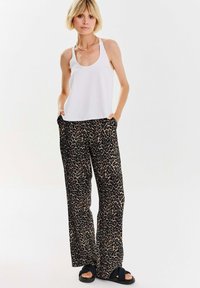 Bílý bezrukávový top kombinovaný s volnými černými kalhotami s leopardím potiskem. Kompletní outfit doplňují pohodlné sandály.