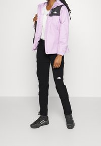 Ljuslila vattentät jacka med svarta accenter, elastiska ärmslut och huva. I kombination med svarta cargobyxor med sidofickor. Mörka skor.