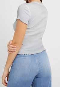 Top corto de manga corta ribeteado en gris claro con un dobladillo ondulado, diseño ajustado y textura suave, combinado con jeans de tiro alto en azul claro.