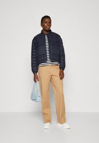 Navy puffy jakke med en cropped design, stripete topp, beige bukser og en lys blå håndveske. Modell som har på seg hvite sneakers.