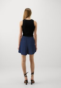 Svart ärmlös topp som matchas med blå högmidjade shorts med bakfickor, slät textur och vid byxdessign.