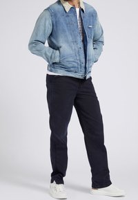 Denim jacket with light wash, beige collar, and front pockets. Paired with dark pants and white sneakers, featuring a simple white shirt underneath.