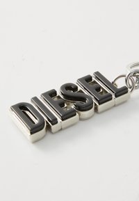 Svart og sølv nøkkelring med ordet "DIESEL" i fete, glinsende bokstaver med metallisk finish; inkluderer en sirkulær festeloop.