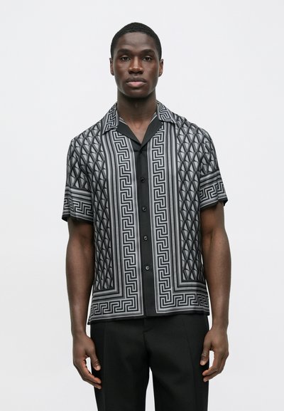 Μαύρο πουκάμισο με κοντά μανίκια και γεωμετρικό γκρι μοτίβο, με μπροστινό κουμπί και αντίθετο γιακά. Το ύφασμα έχει απαλή υφή.